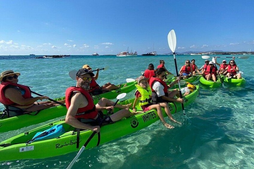 People kayaking on turquoise water, wearing life jackets and paddling in green kayaks. 2