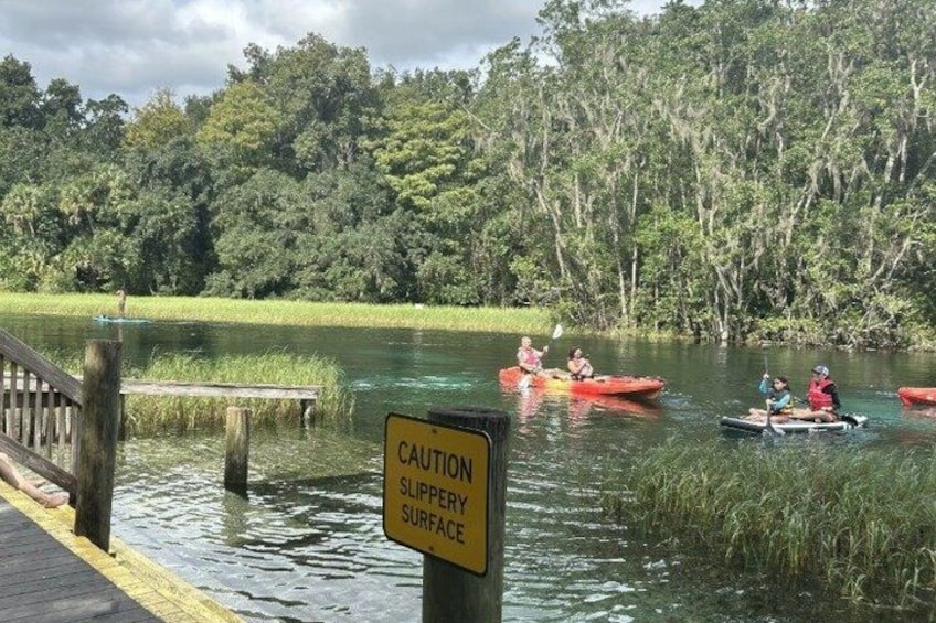A river with kayakers, a caution sign, and a dock. 1