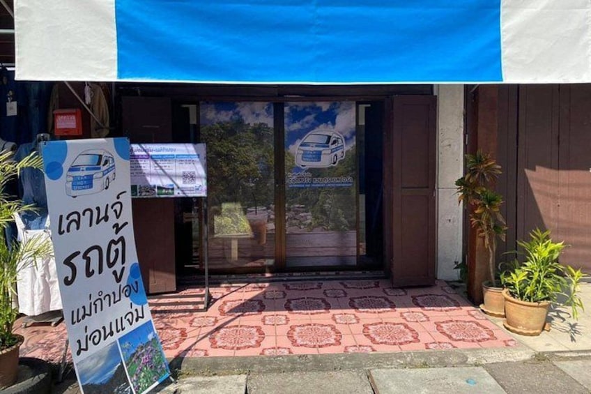 A building entrance with a blue awning, a signboard, and potted plants. 5