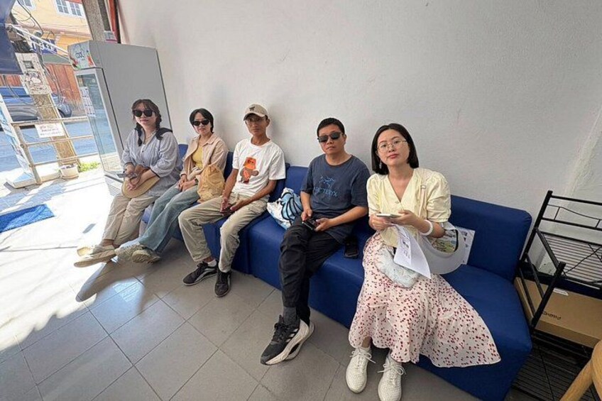 A group of people sitting on a blue couch in a room with a window and a door. 4