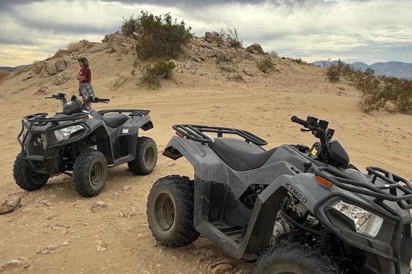 Two ATVs parked on a dirt trail with a person standing in the background. 3