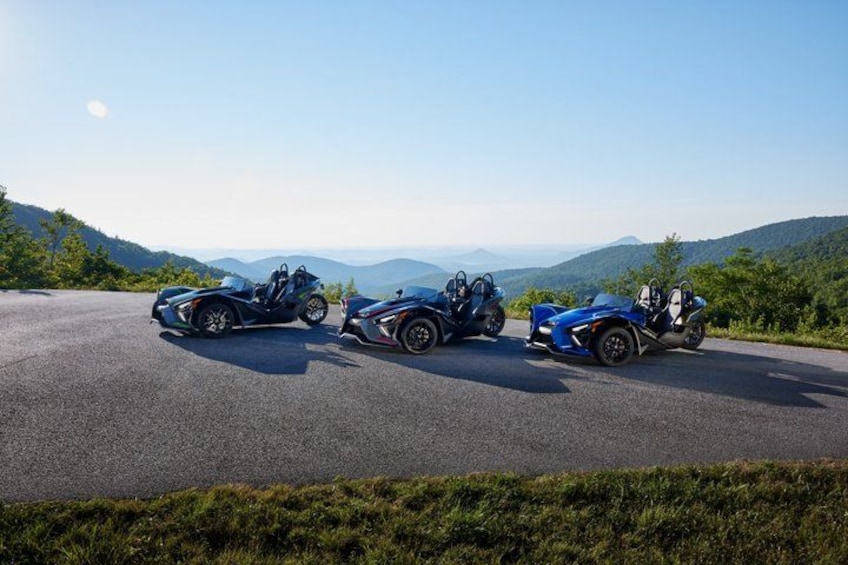 Three blue sports cars parked on a road with a mountainous landscape in the background. 1