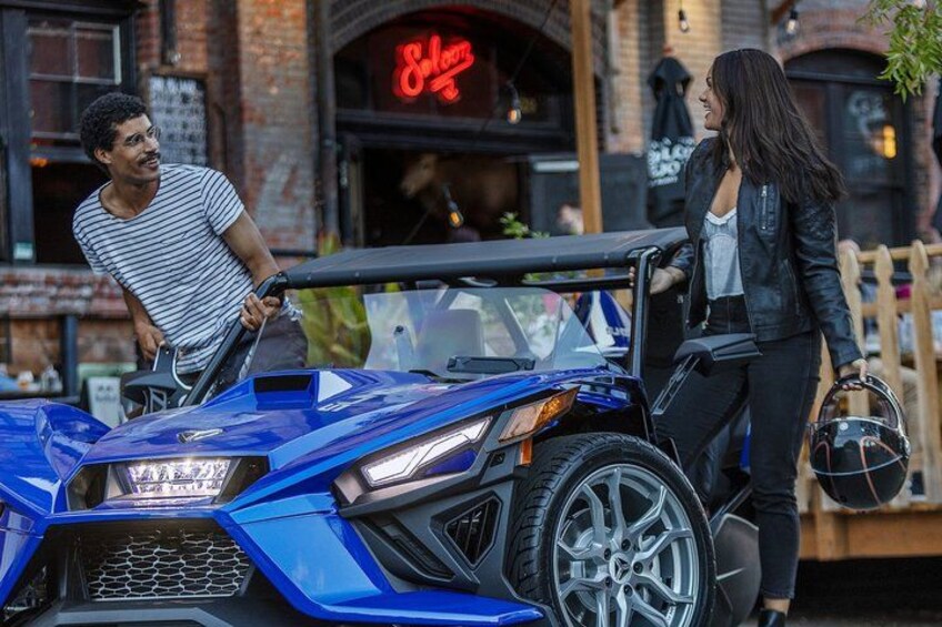 A blue sports car parked on a street with a brick building in the background. 3