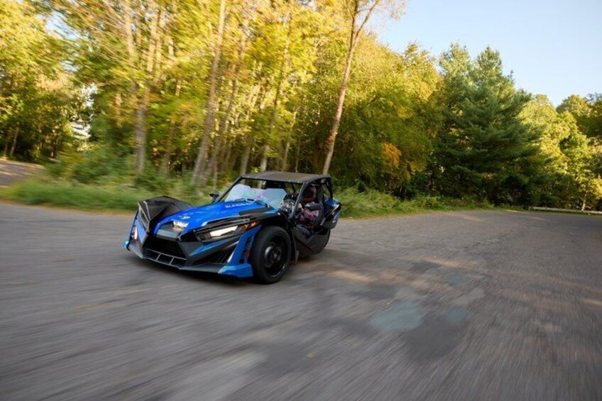 A blue sports car driving on a road surrounded by trees. 2
