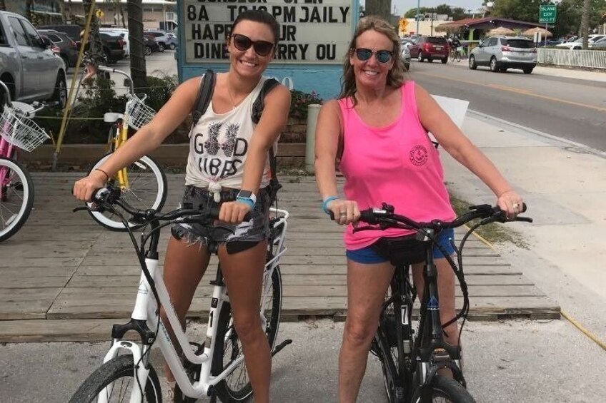 Two people on bicycles on a sidewalk with a sign in the background. 5