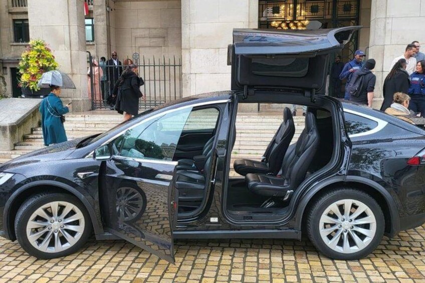 A black car with its door open, parked on a cobblestone street. 4