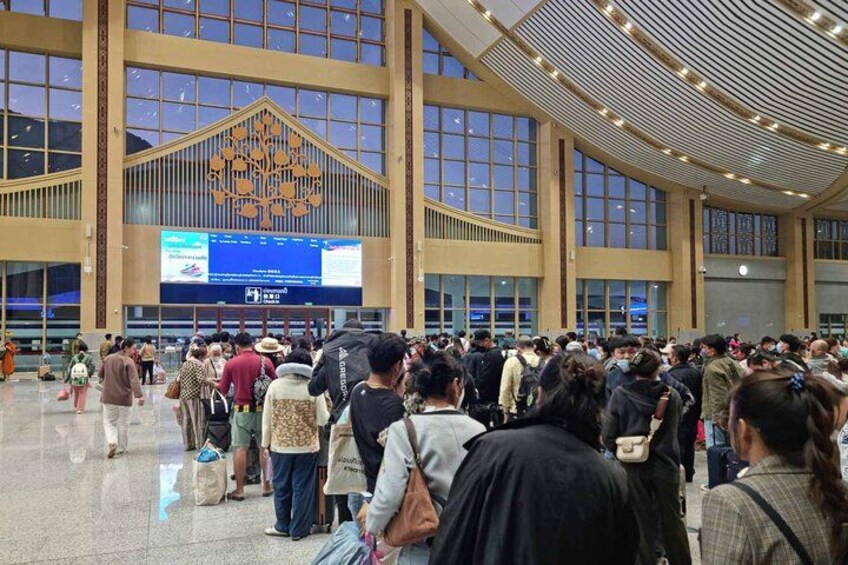 A crowded indoor space with large windows and a digital display board. 5