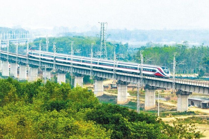 A high-speed train crossing a long bridge over a river, surrounded by greenery. 2