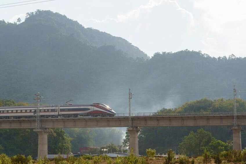 A train crossing a bridge over a river with mountains in the background. 3