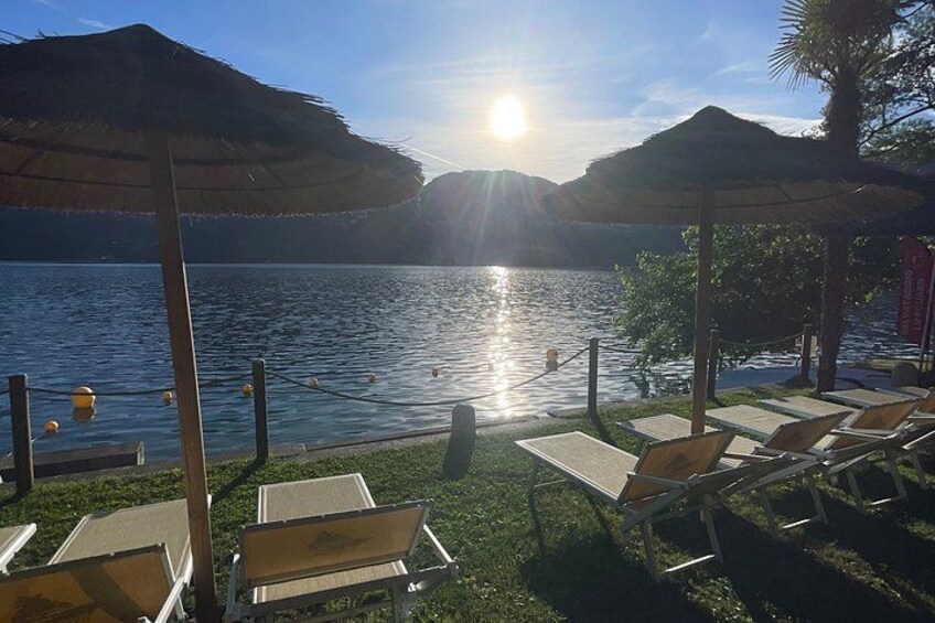 A lakeside setting with sunlit water, lounge chairs, and thatched umbrellas. 3
