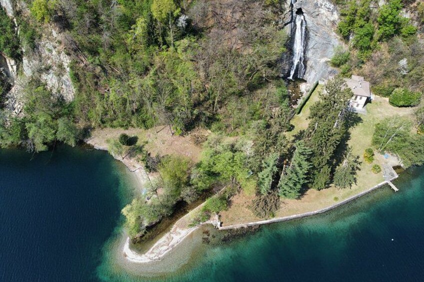 An aerial view of a coastal area with a waterfall, a beach, and a house surrounded by trees. 1