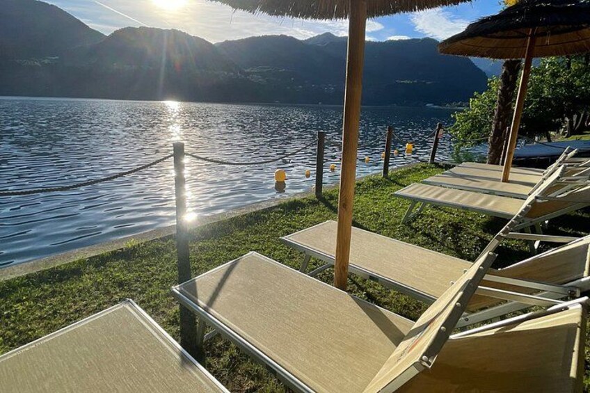 A lakeside lounge with sun loungers, a rope barrier, and mountains in the background. 4