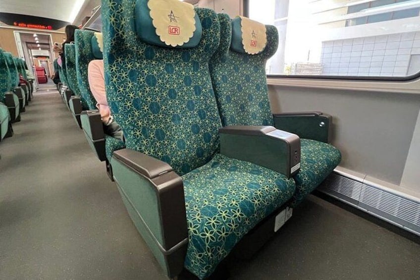 A row of green patterned seats with a headrest and a small pillow on each. 4