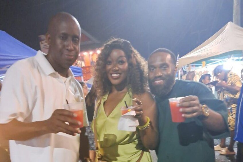 Three people holding drinks at an outdoor event with tents in the background. 2