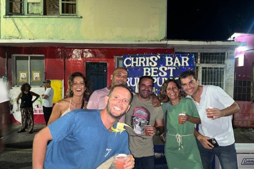 A group of people standing in front of a bar named 'Chris's Bar Best Rum Punch.' 4
