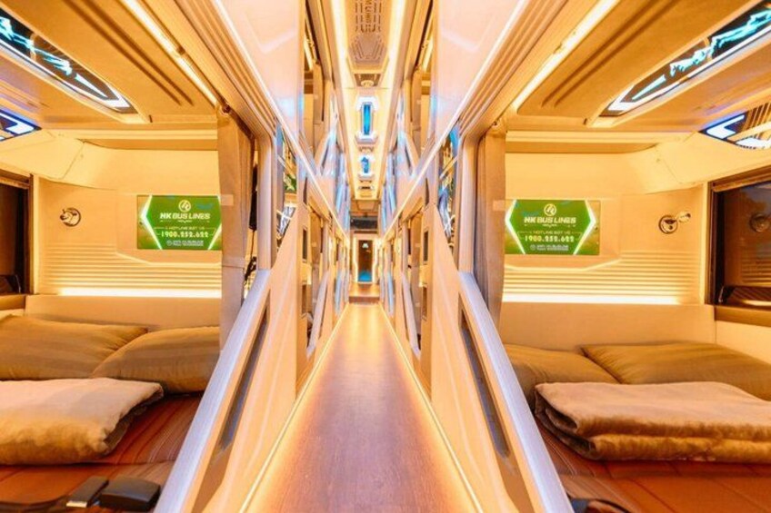 A train interior with a central aisle, seating on either side, and overhead luggage compartments. 1