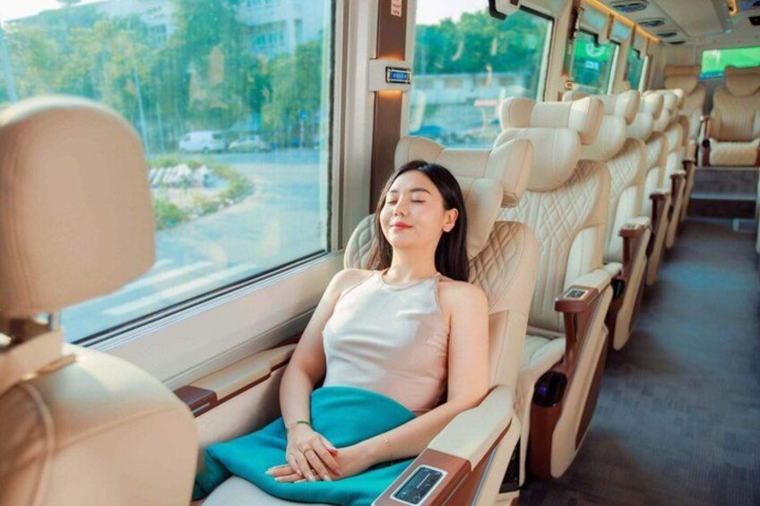 A person seated in a bus, with windows showing a road and greenery outside. 5