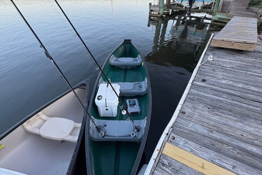 A small boat docked at a wooden pier with fishing rods. 3
