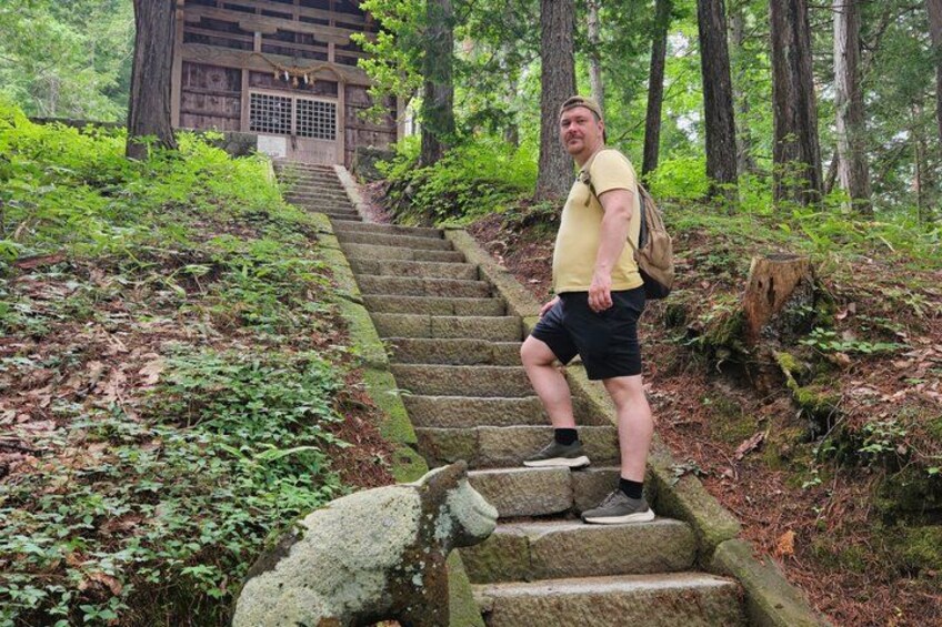 A person climbing stone steps in a forested area with a traditional wooden structure in the background. 4