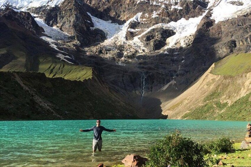 A person standing in a clear lake surrounded by mountains with snow-capped peaks. 1