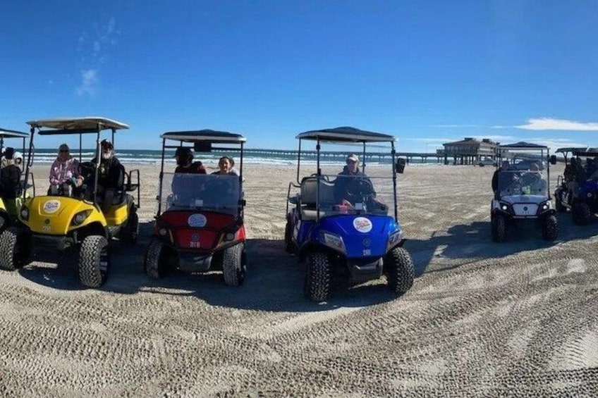 Golf carts parked on a sandy beach with the ocean in the background. 2