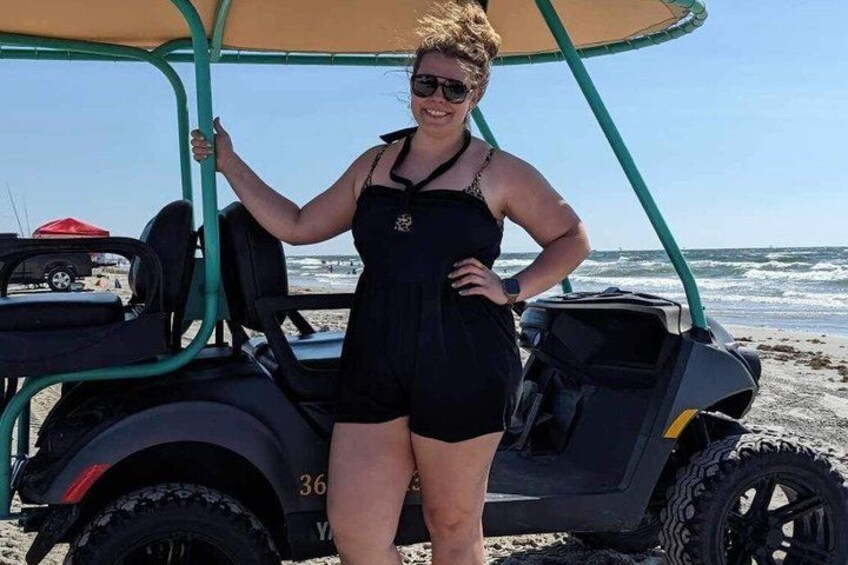 A person standing next to a golf cart on a beach with the ocean in the background. 5