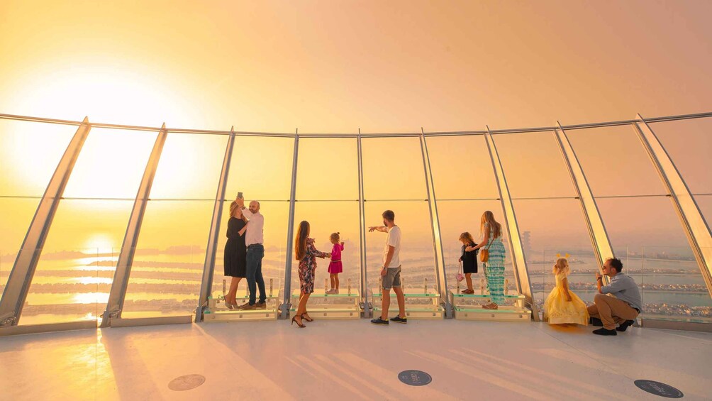 A group of people at a glass observation deck overlooking a cityscape during sunset. 3