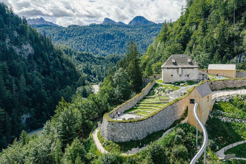 Un paysage montagneux avec un mur de soutènement en pierre, un bâtiment en bois et une route sinueuse. 1