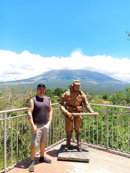 Un hombre está de pie junto a una estatua en un balcón con vistas a un paisaje montañoso. 5