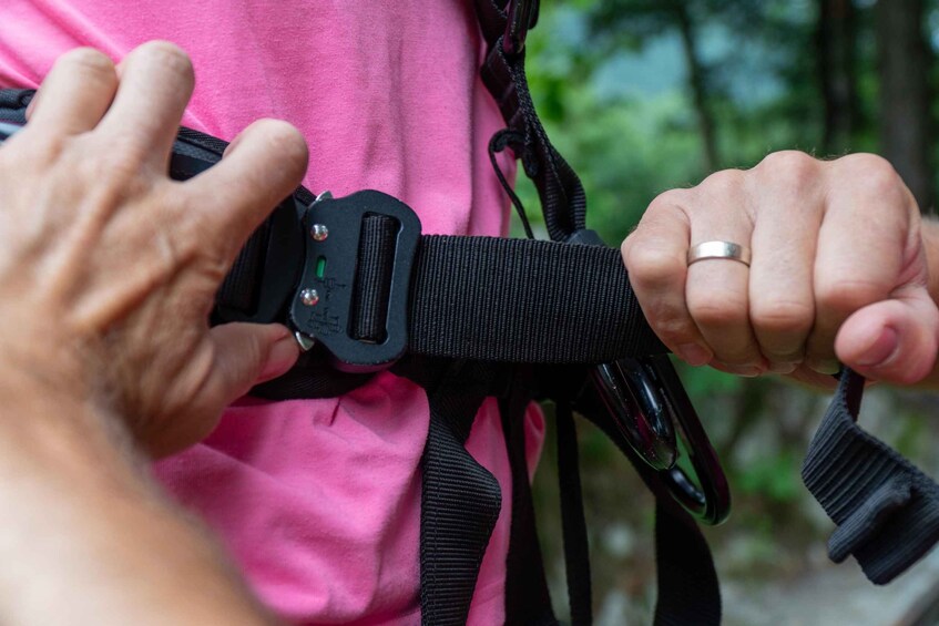 A person wearing a pink shirt and securing a black harness with a buckle. 5