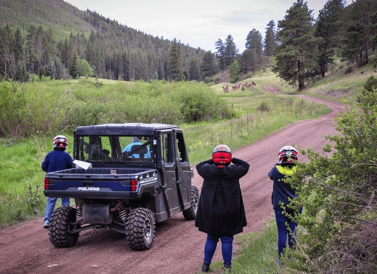 A black off-road vehicle on a dirt road with three people wearing helmets, one taking a photo. 4