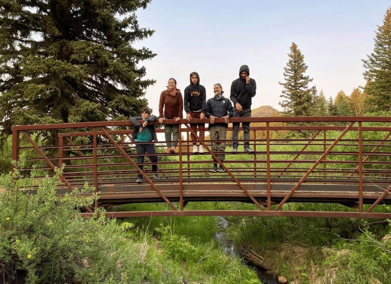 A group of people standing on a metal bridge over a stream in a forested area. 2