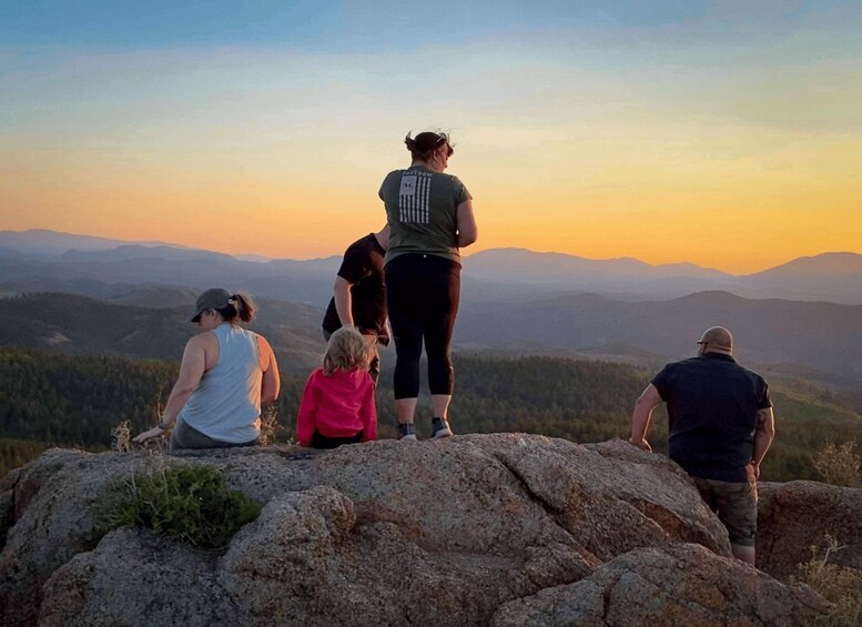 A group of people standing on a rocky outcrop overlooking a mountainous landscape during sunset. 3