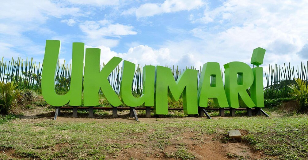 De grandes lettres vertes épellent le mot « UKUMARI » sur un champ d’herbe, avec une clôture en arrière-plan. 5