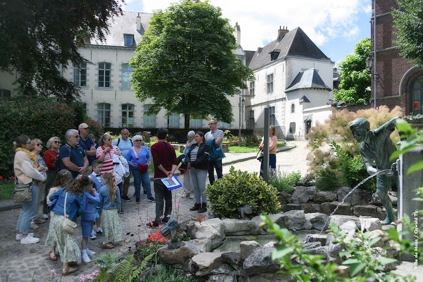 Un grupo de personas reunidas en un patio con una estatua, rodeado de muros de piedra y vegetación. 2