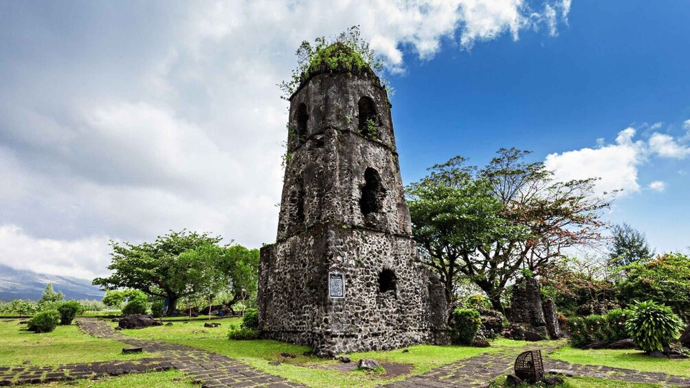 An ancient stone tower with a plaque, surrounded by lush greenery and a clear sky. 3