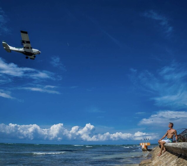 Un petit avion survole une plage, et on aperçoit une personne assise sur un rocher. 5