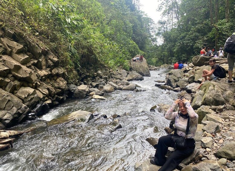 Un arroyo pedregoso con gente sentada sobre las rocas tomando fotografías. 3