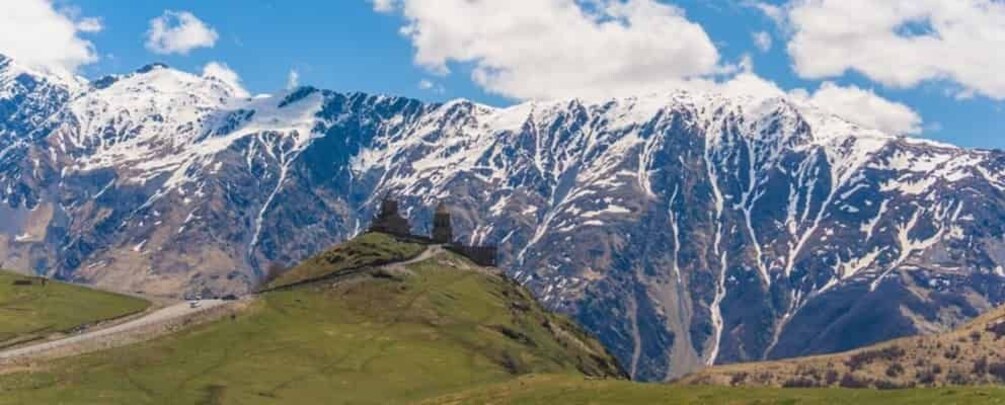Une chaîne de montagnes aux sommets enneigés, une vallée verdoyante et une petite structure ressemblant à une tour. 4