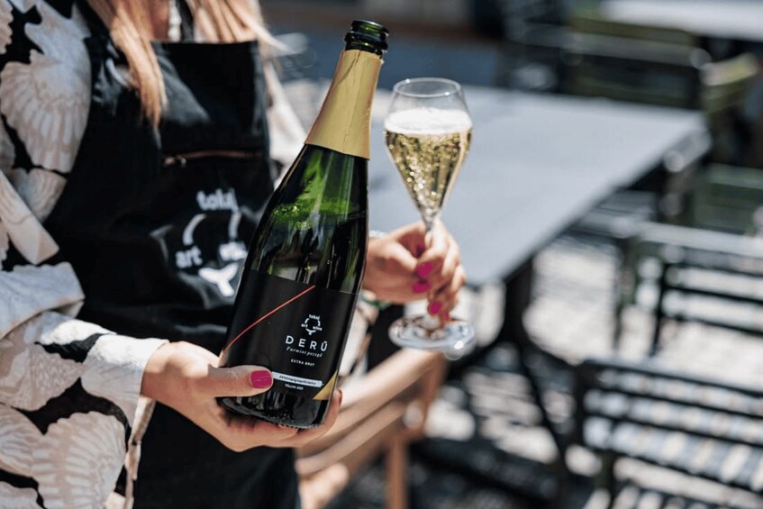 Iemand houdt een fles Derú-wijn en een glas champagne vast. 1