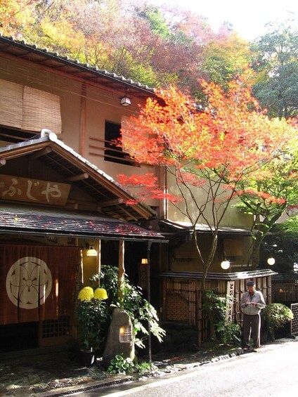 Un bâtiment traditionnel japonais, avec une enseigne, un arbre aux feuilles d’automne et une personne debout près de l’entrée. 1