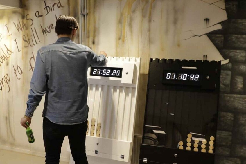 Une personne tenant une bouteille, debout devant un mur orné d’une horloge et d’une étagère remplie de bouteilles. 4