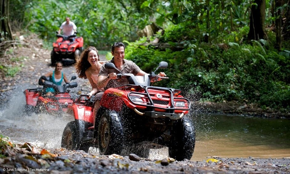 Des personnes conduisent des quads sur un chemin boueux, et l'eau éclabousse tout autour. 1