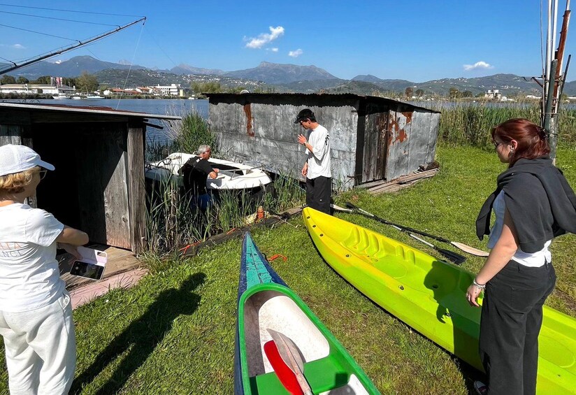 A group of people near a body of water with canoes, a small shed, and a mountainous landscape in the background. 4