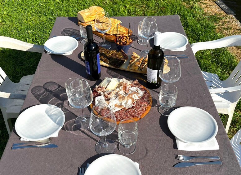 An outdoor picnic setup with a table set for two, featuring a charcuterie board, bread, and wine glasses. 2