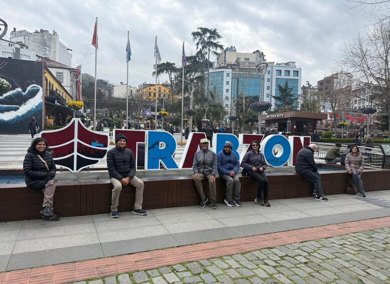 A group of people sitting on a bench in front of a large sign with the word 'STRATOV' and a wave mural in the background. 4