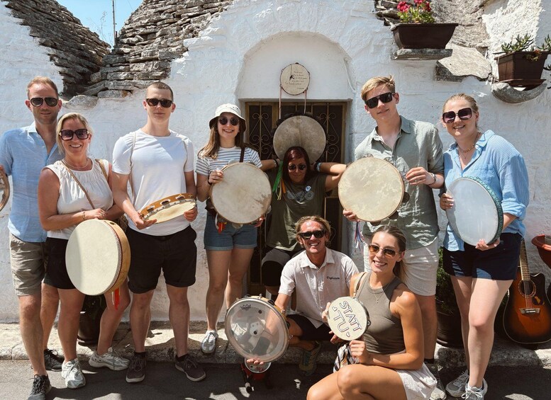 A group of people holding drums in front of a white building with a stone roof. 1