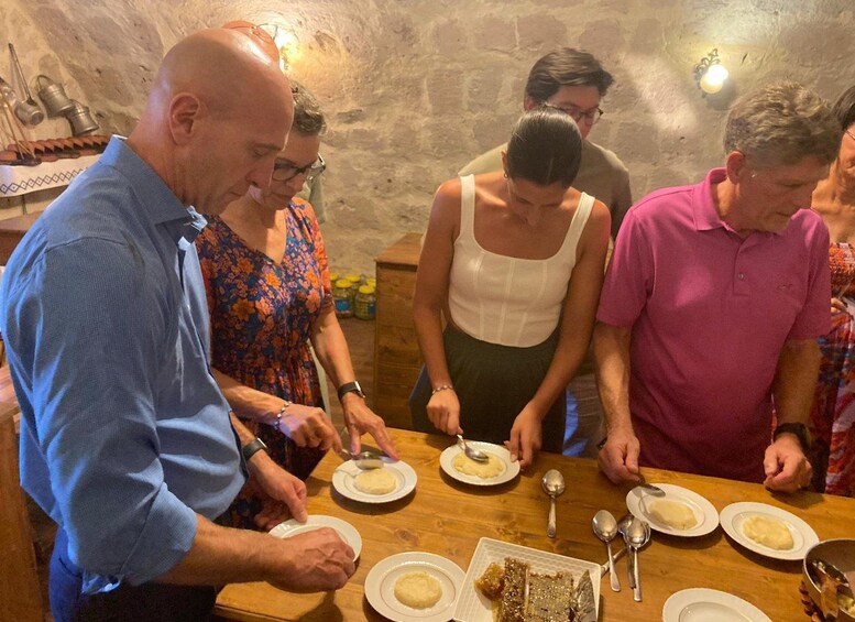 A group of people dining at a wooden table in a rustic setting with stone walls. 1