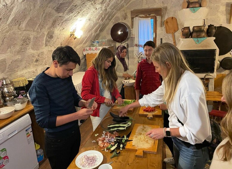 A group of people preparing food in a rustic kitchen with stone walls and traditional cookware. 3