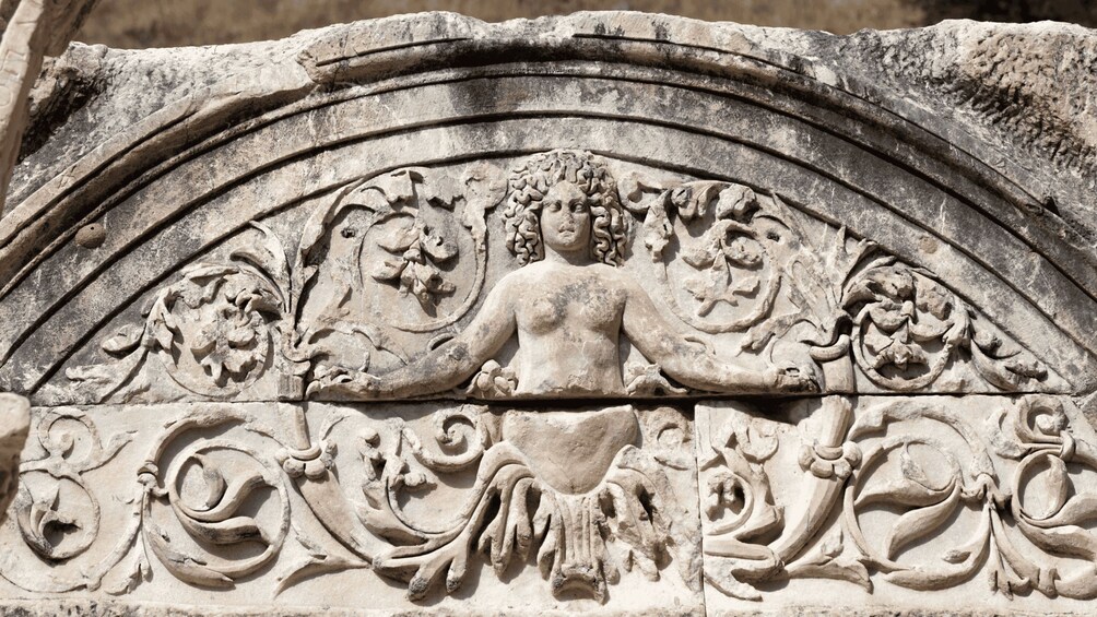 Un detallado relieve de piedra con una figura central, intrincados motivos florales y un arco curvo. 5